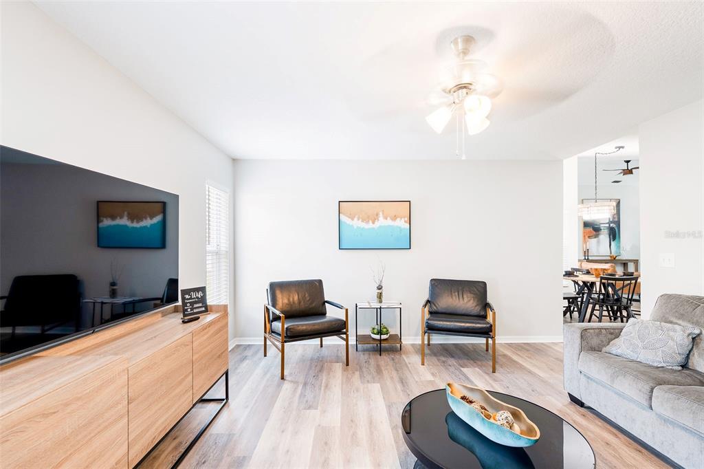 A living room features light wood flooring, two black leather chairs, and a large television — 11225 FLOWER AVENUE, WEEKI WACHEE, FL