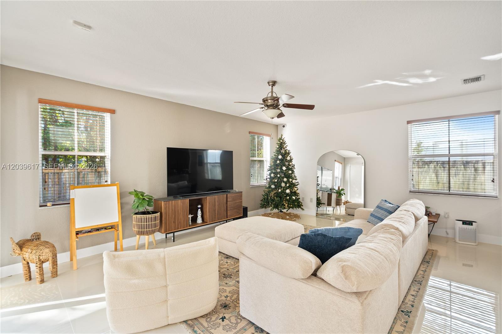 A living room features a beige sectional sofa, a television on a console, and a tree — 11558 NW 84th  St, Doral FL 33178, DORAL, FL