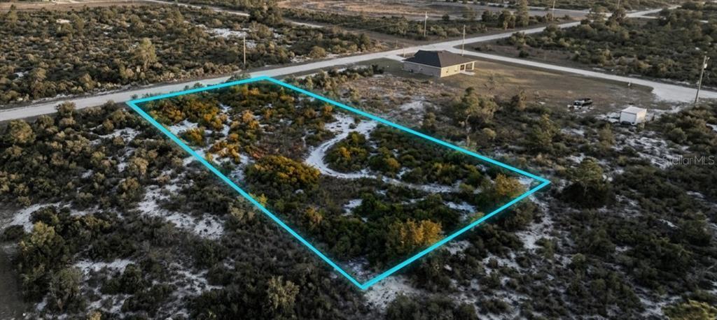 An aerial view shows a vacant, rectangular plot of land outlined in blue near a road — 1028 S LANDRY ROAD, AVON PARK, FL