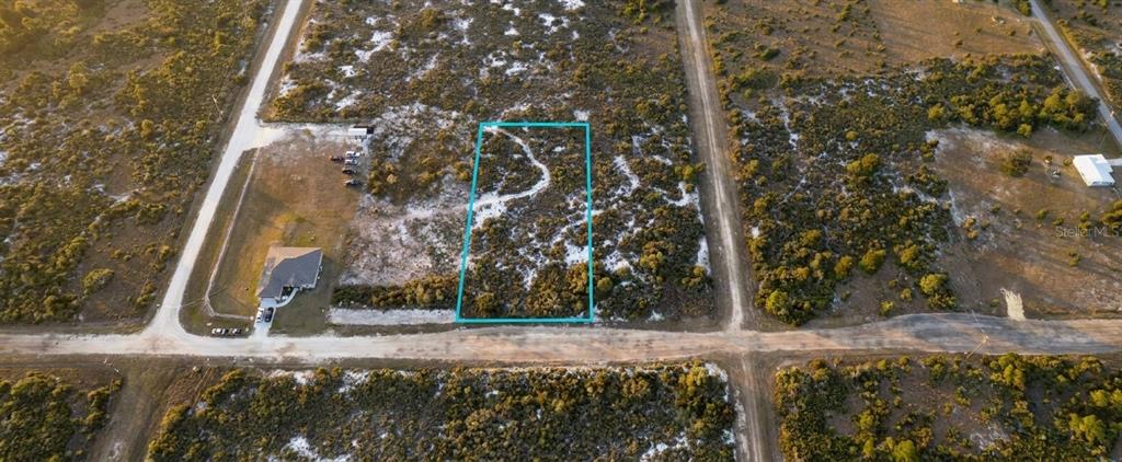 An aerial view shows a vacant rectangular lot outlined in blue between two dirt roads — 1028 S LANDRY ROAD, AVON PARK, FL