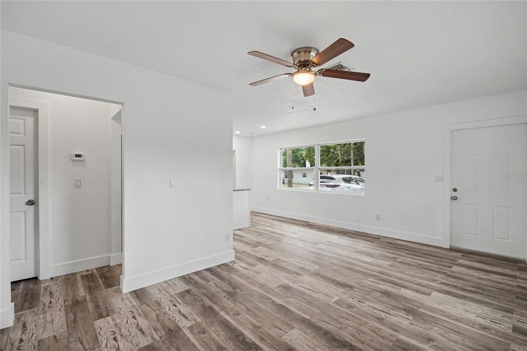 A bright, empty room features white walls, wood-look flooring, a ceiling fan, and two doors — 1423 18TH STREET W, BRADENTON, FL