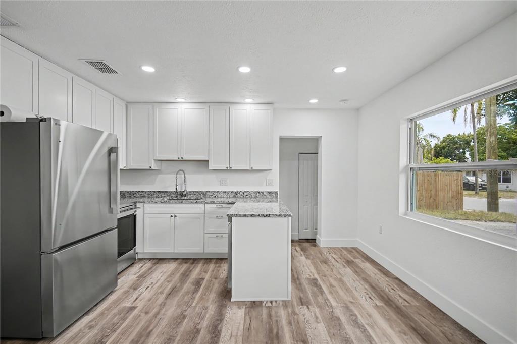 A modern kitchen features white cabinets, granite countertops, stainless steel appliances, and wood-look flooring — 1423 18TH STREET W, BRADENTON, FL