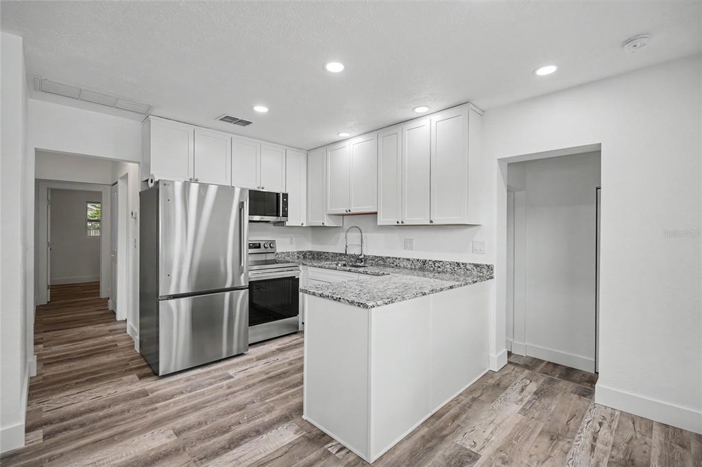 A kitchen with white cabinets, granite countertops, stainless steel appliances, and wood-look flooring — 1423 18TH STREET W, BRADENTON, FL