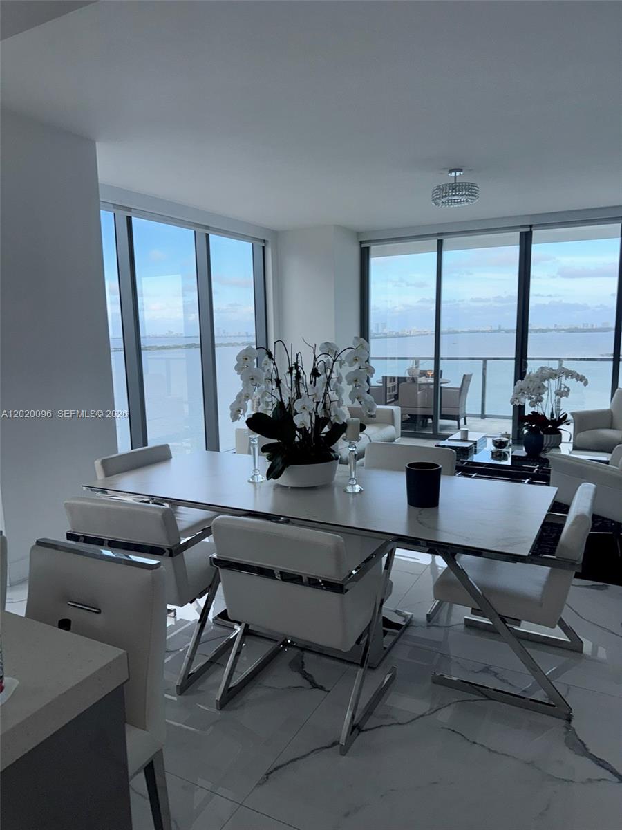 A modern dining area features a white table, chrome-framed chairs, and floor-to-ceiling windows overlooking water — 788 NE 23rd St # 1202, Miami FL 33137, MIAMI, FL