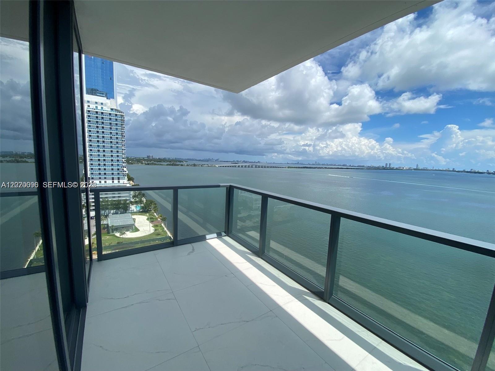 A balcony with white tile flooring and glass railings overlooks a bay and city skyline — 788 NE 23rd St # 1202, Miami FL 33137, MIAMI, FL