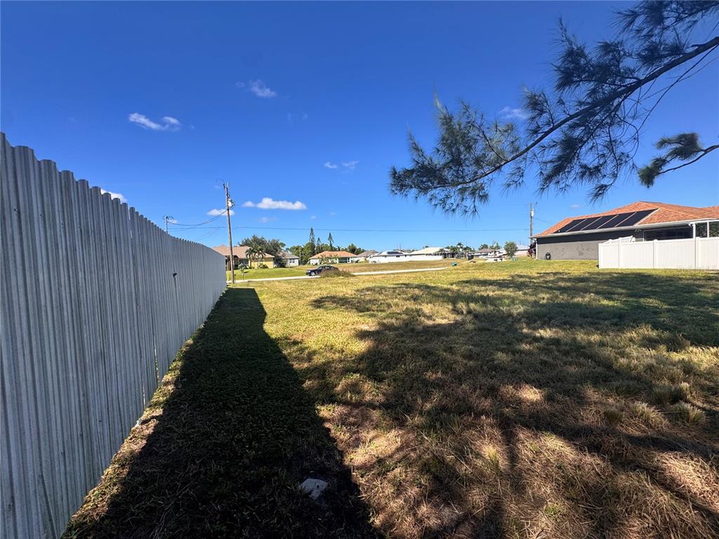 A grassy vacant lot sits between two residential properties with white vinyl fences — 1211 NW 21ST AVENUE, CAPE CORAL, FL