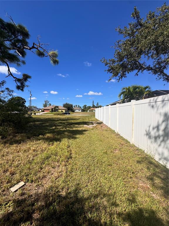 A grassy vacant lot sits next to a white vinyl privacy fence under a blue sky — 1211 NW 21ST AVENUE, CAPE CORAL, FL