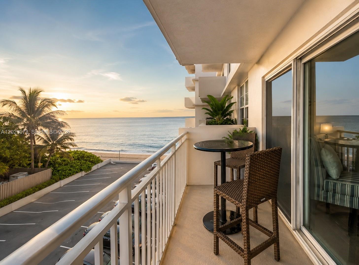 A balcony with a bistro set overlooks a parking lot, beach, and the ocean at sunset — 4505 S Ocean Blvd # 502, Highland Beach FL 33487, HIGHLAND BEACH, FL