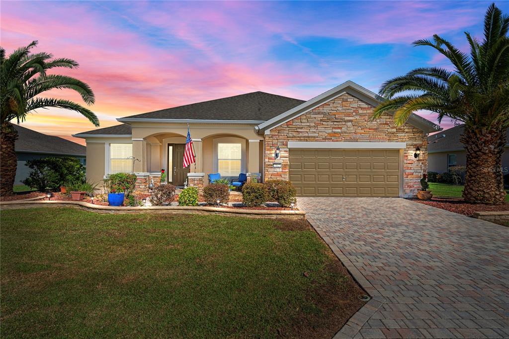 A single-story house with a stone facade, a paved driveway, and palm trees at sunset — 7527 SW 97TH TERRACE ROAD, OCALA, FL