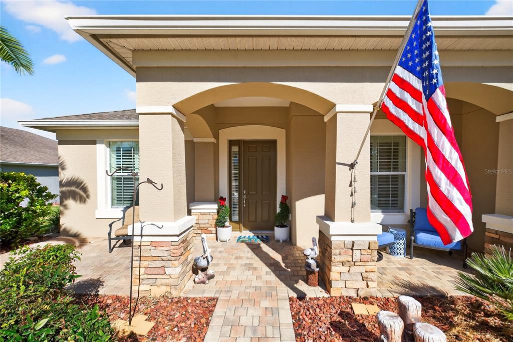 The exterior of a house features a covered porch with stone columns and an American flag — 7527 SW 97TH TERRACE ROAD, OCALA, FL