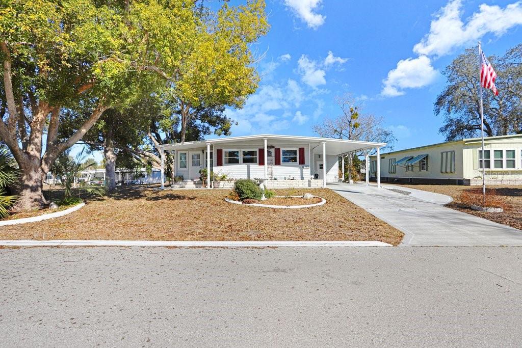 A single-story mobile home with a carport, white siding, and red shutters under a blue sky — 14299 NECTARINE STREET, BROOKSVILLE, FL