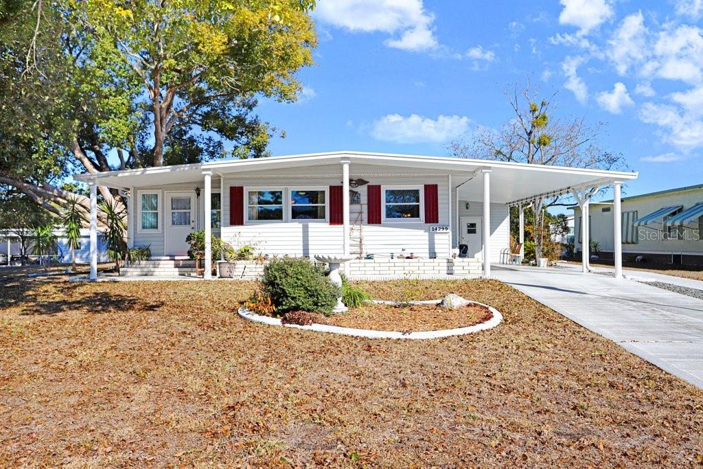 A single-story manufactured home features white siding, red shutters, and an attached carport — 14299 NECTARINE STREET, BROOKSVILLE, FL