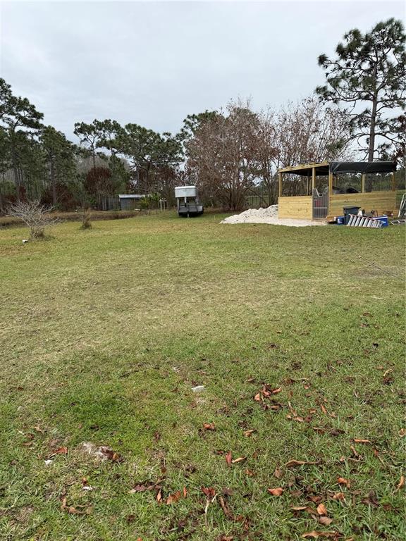 A grassy backyard features a horse trailer, a wooden structure, and scattered trees — 3811 BANCROFT BOULEVARD, ORLANDO, FL