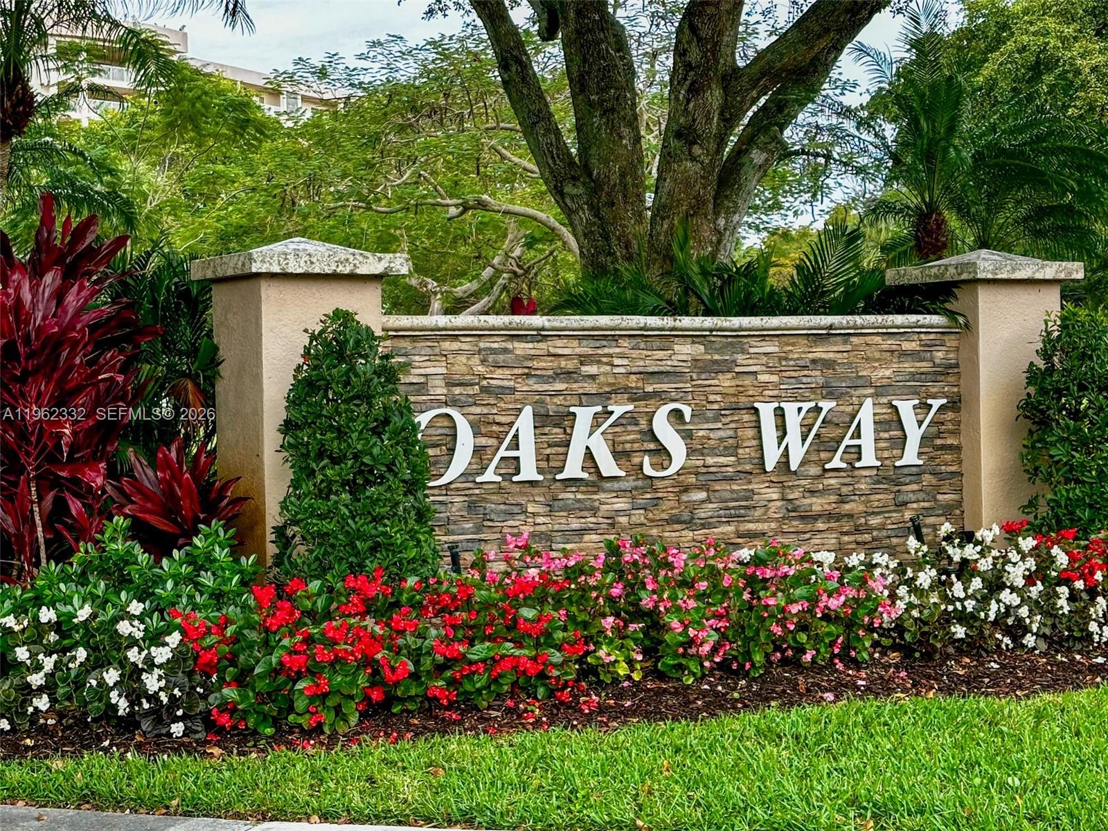 A stone monument sign with the text OAKS WAY sits in a landscaped garden — 3510 Oaks Way # 408, Pompano Beach FL 33069, POMPANO BEACH, FL