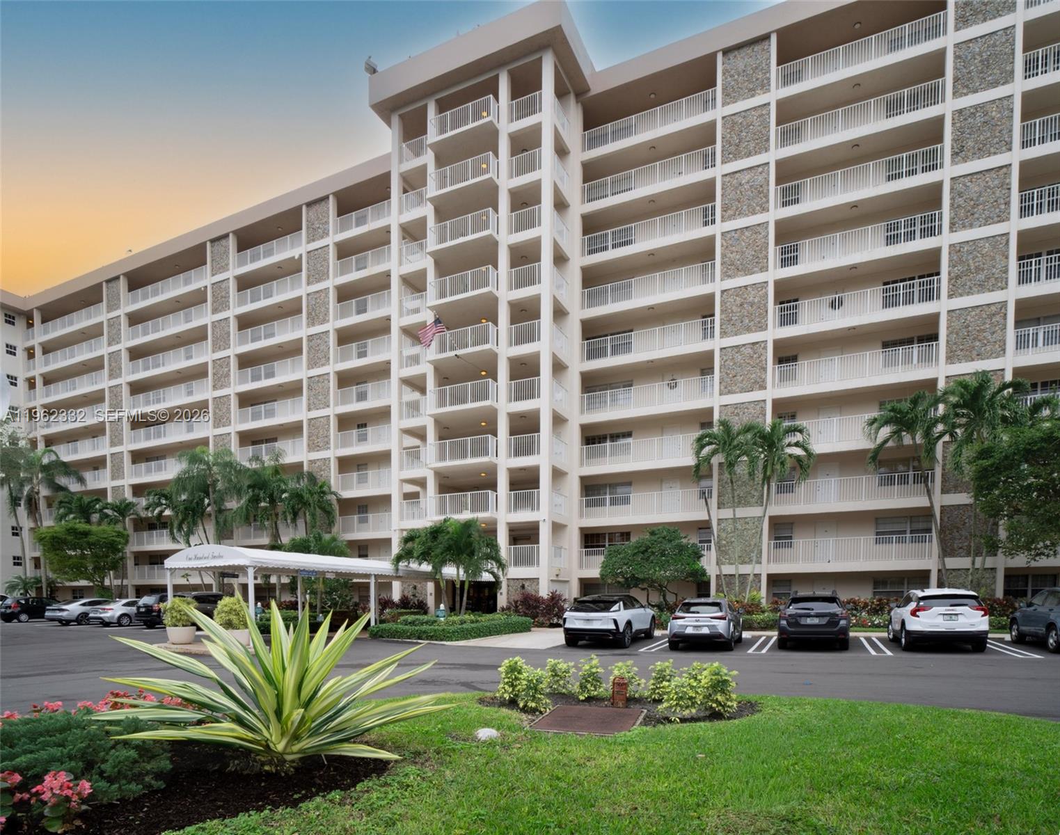 A multi-story residential apartment building features balconies and a parking lot with several cars — 3510 Oaks Way # 408, Pompano Beach FL 33069, POMPANO BEACH, FL