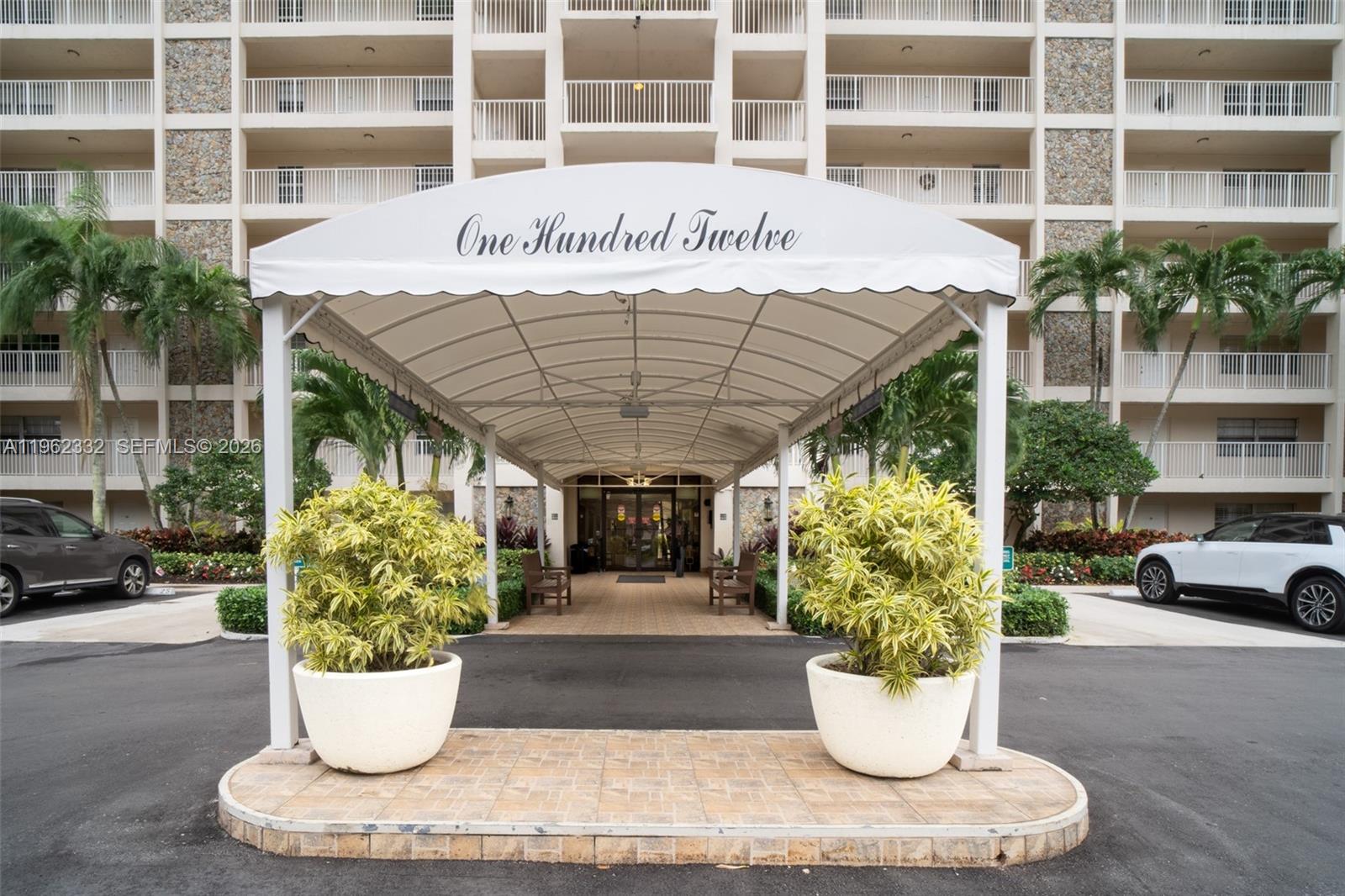 The exterior entrance of a multi-story residential building features a covered walkway and potted plants — 3510 Oaks Way # 408, Pompano Beach FL 33069, POMPANO BEACH, FL