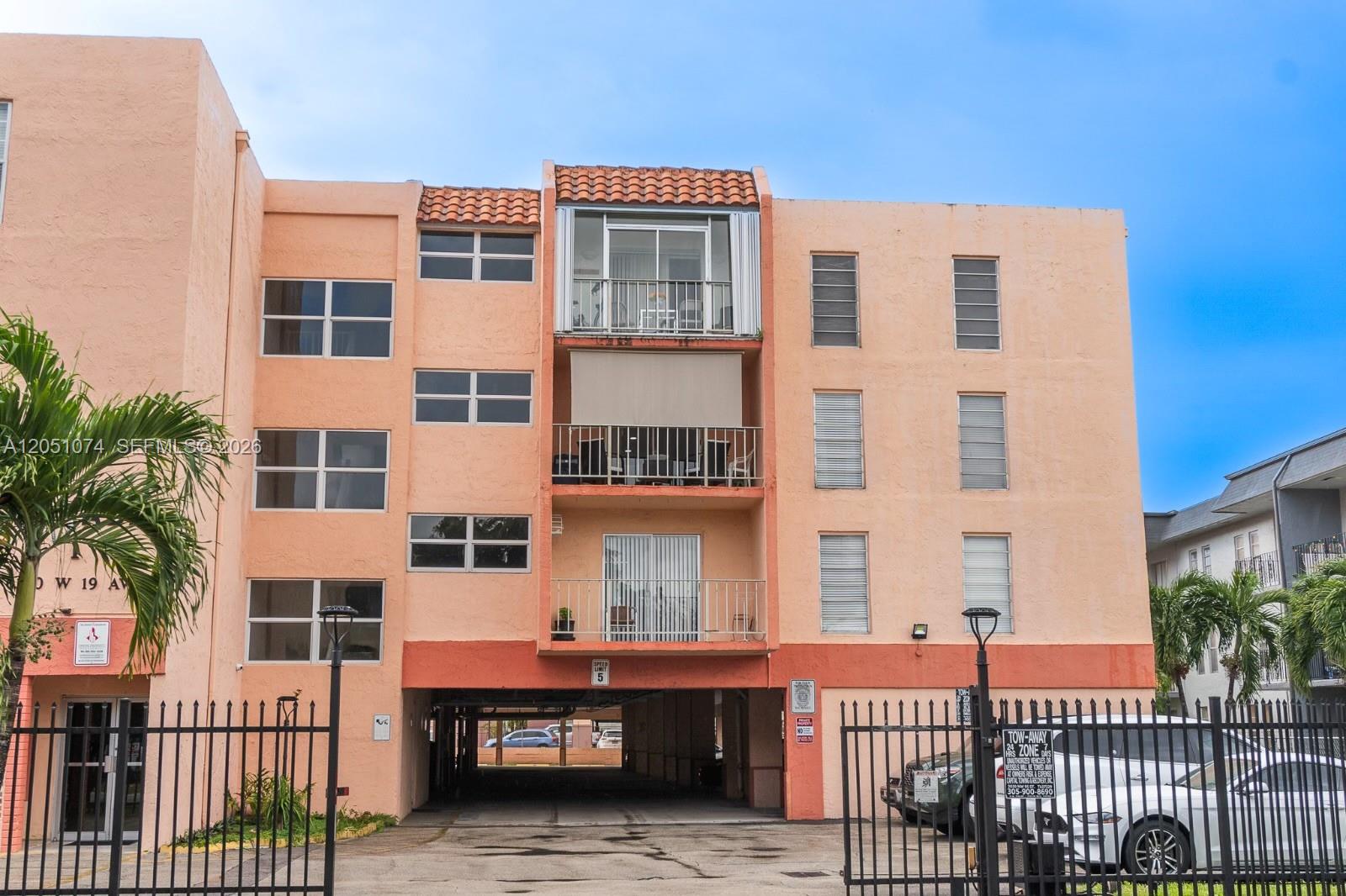 The exterior of a multi-story peach-colored apartment building features balconies and a ground-level parking area — 6190 W 19th Ave # 201, Hialeah FL 33012, HIALEAH, FL