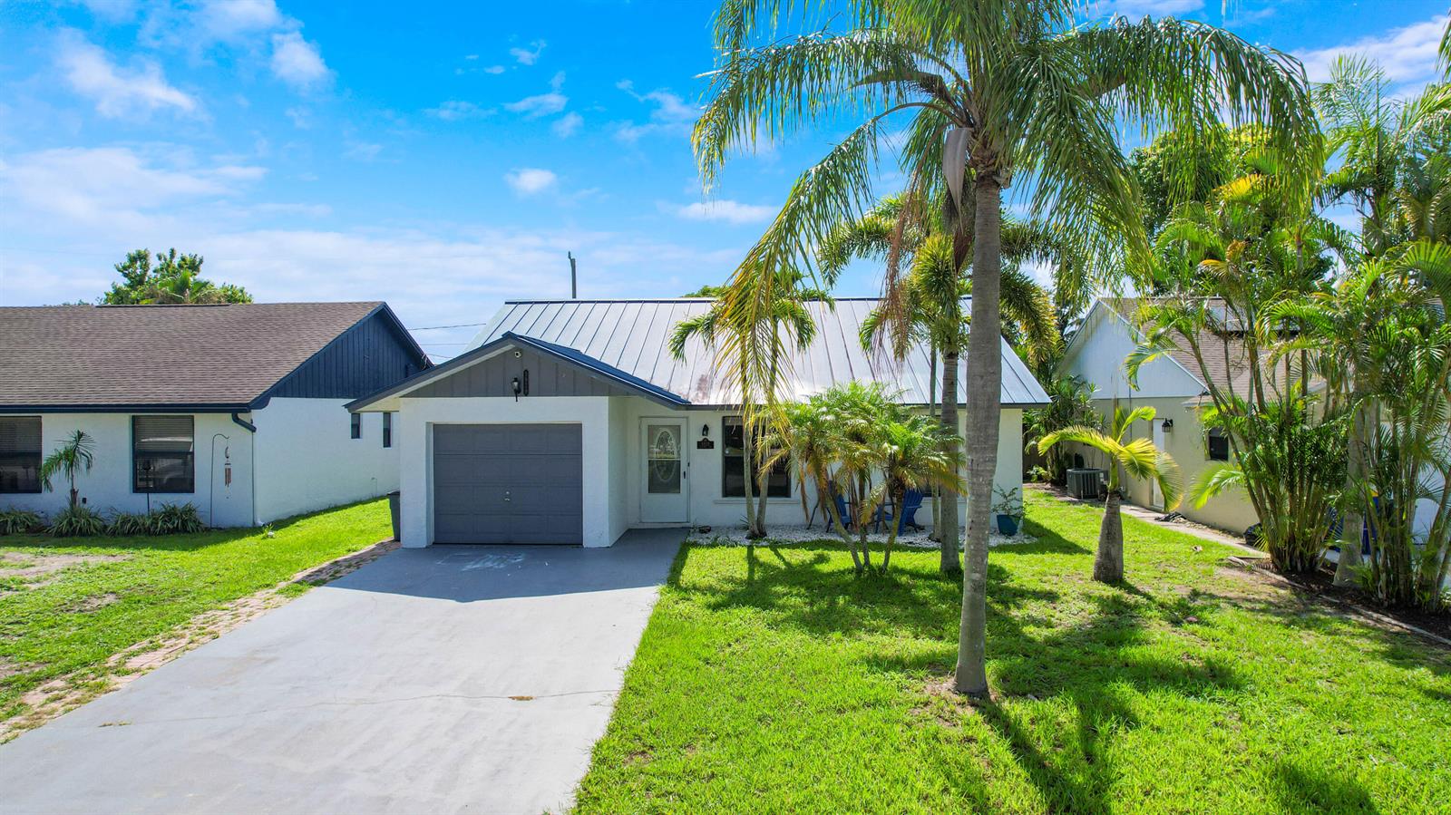 A single-story house with a metal roof, a one-car garage, and palm trees in front — 5929 SE Collins Avenue, Stuart FL 34997, STUART, FL