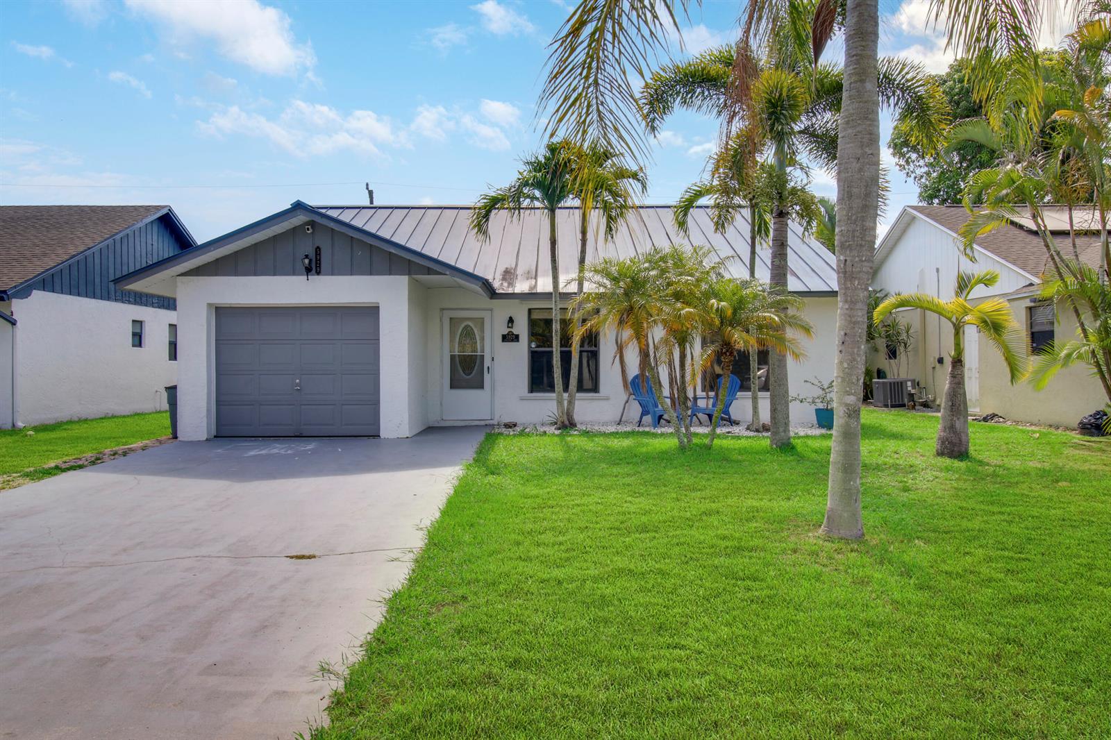 A single-story house with a grey garage, metal roof, and palm trees in the front yard — 5929 SE Collins Avenue, Stuart FL 34997, STUART, FL