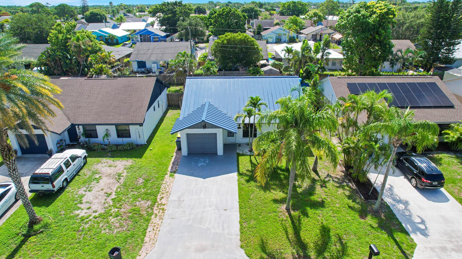 An aerial view shows three suburban houses with driveways, palm trees, and a metal roof — 5929 SE Collins Avenue, Stuart FL 34997, STUART, FL