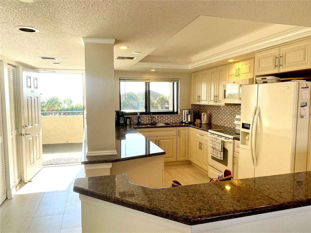 A kitchen features granite countertops, cream-colored cabinetry, white appliances, and an adjacent balcony door — 1290 GULF BOULEVARD UNIT 302, CLEARWATER, FL