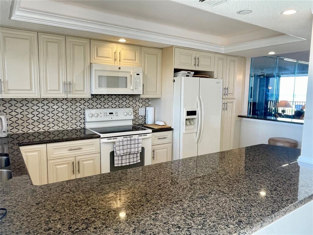A kitchen features cream cabinets, granite countertops, a patterned backsplash, and white appliances — 1290 GULF BOULEVARD UNIT 302, CLEARWATER, FL