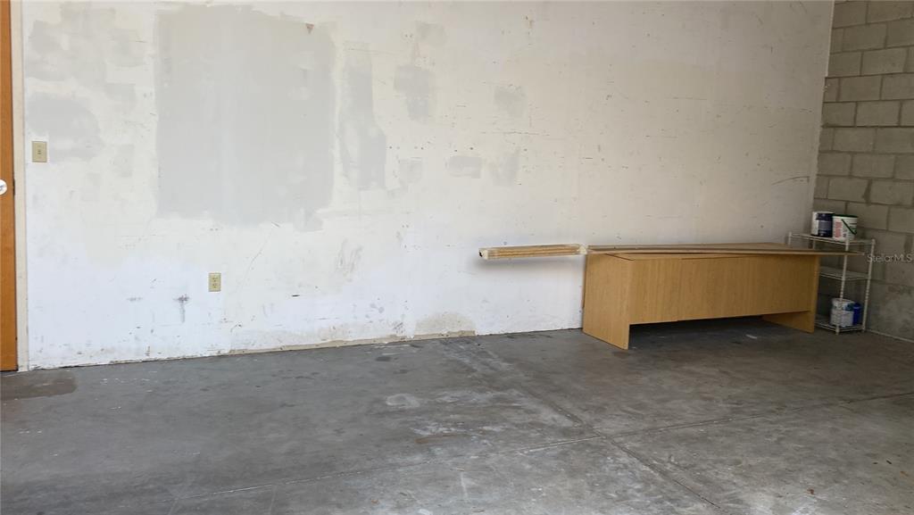 An unfinished garage features a concrete floor, a light-colored wall, and a wooden desk — 1500 TROPIC PARK DRIVE UNIT 1582, SANFORD, FL