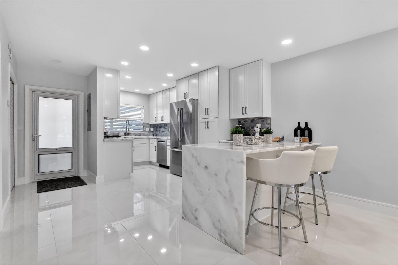 A modern kitchen features white cabinetry, marble countertops, a waterfall island, and glossy tile floors — 700 NE Harbour Terrace # 1250, Boca Raton FL 33431, BOCA RATON, FL