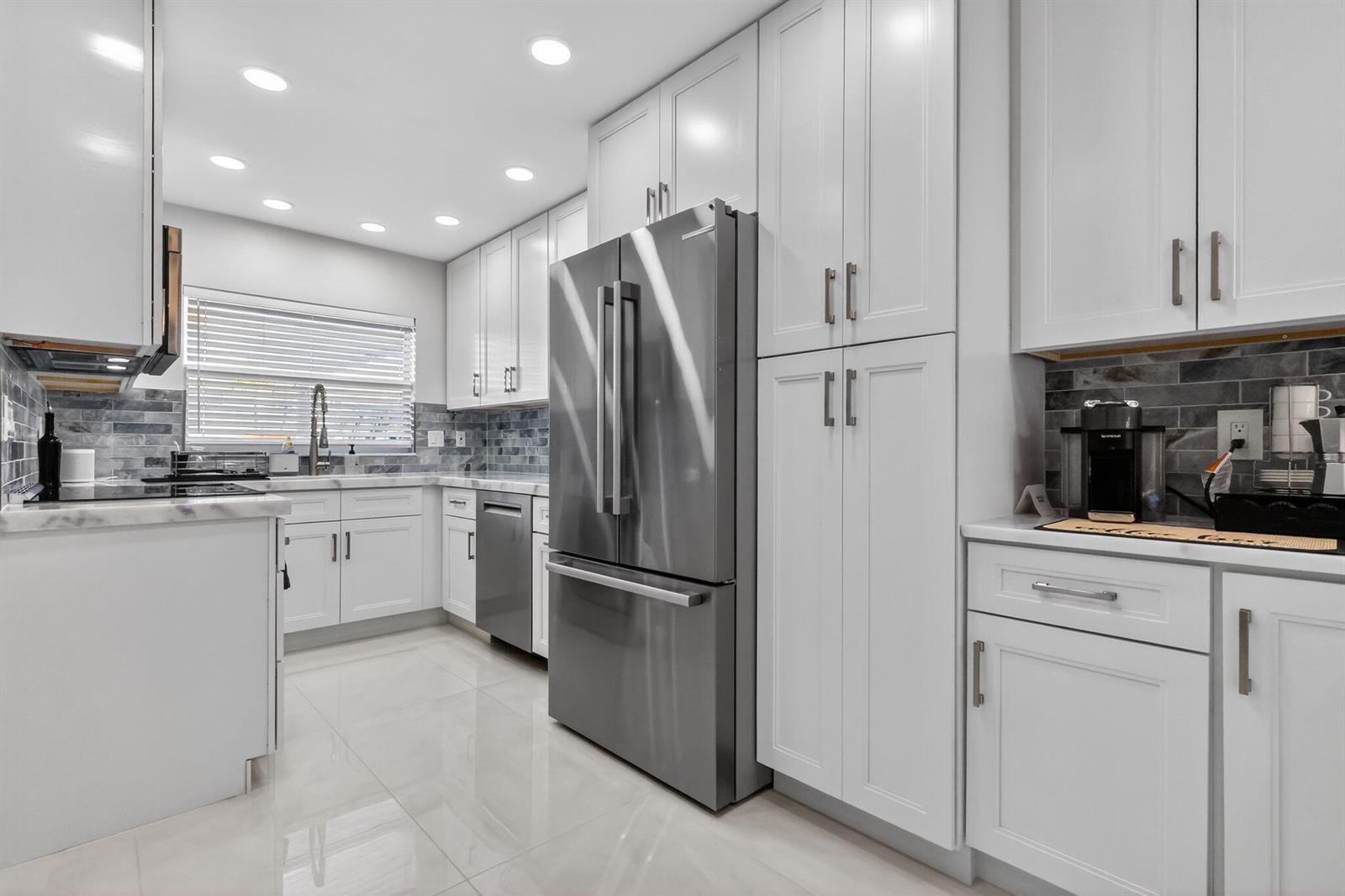 A modern kitchen features white cabinets, stainless steel appliances, and a gray tiled backsplash — 700 NE Harbour Terrace # 1250, Boca Raton FL 33431, BOCA RATON, FL