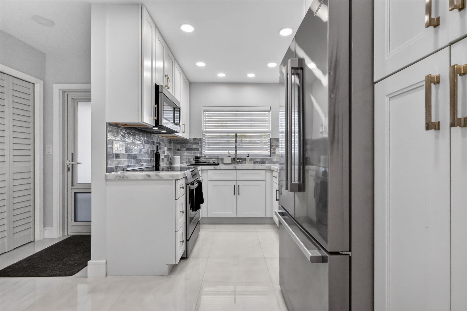 A modern kitchen features white cabinetry, stainless steel appliances, and a gray tiled backsplash — 700 NE Harbour Terrace # 1250, Boca Raton FL 33431, BOCA RATON, FL