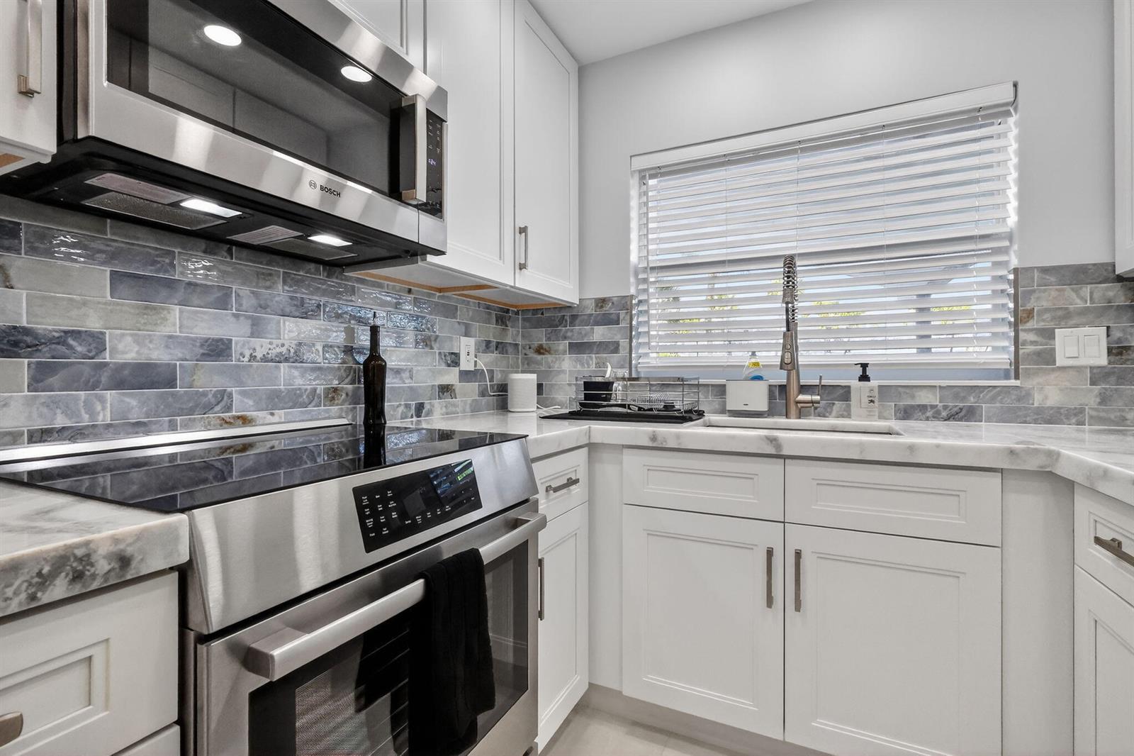 A modern kitchen features white cabinets, stainless steel appliances, and a blue-toned subway tile backsplash — 700 NE Harbour Terrace # 1250, Boca Raton FL 33431, BOCA RATON, FL