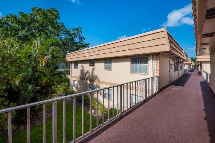 An exterior view of a two-story apartment building with a long, elevated walkway and railing — 657 Brittany N, Delray Beach FL 33446, DELRAY BEACH, FL