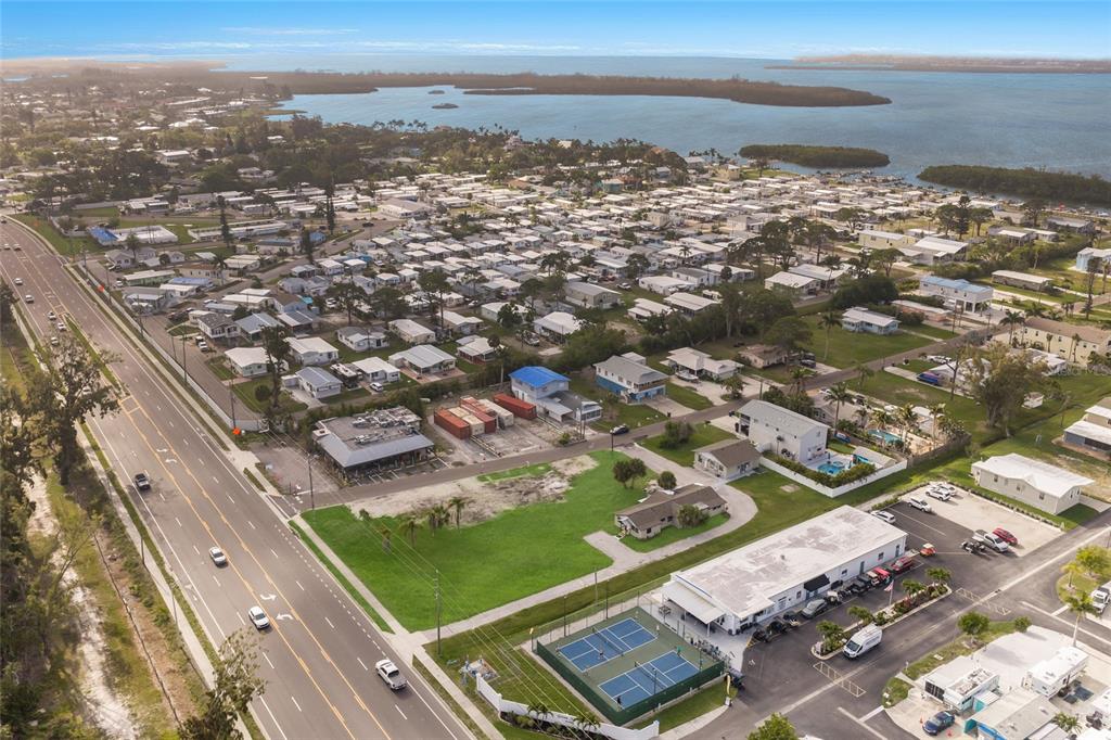 An aerial view shows a coastal neighborhood with a tennis court, parking lot, and road — 10601-10611 CORTEZ ROAD W, BRADENTON, FL