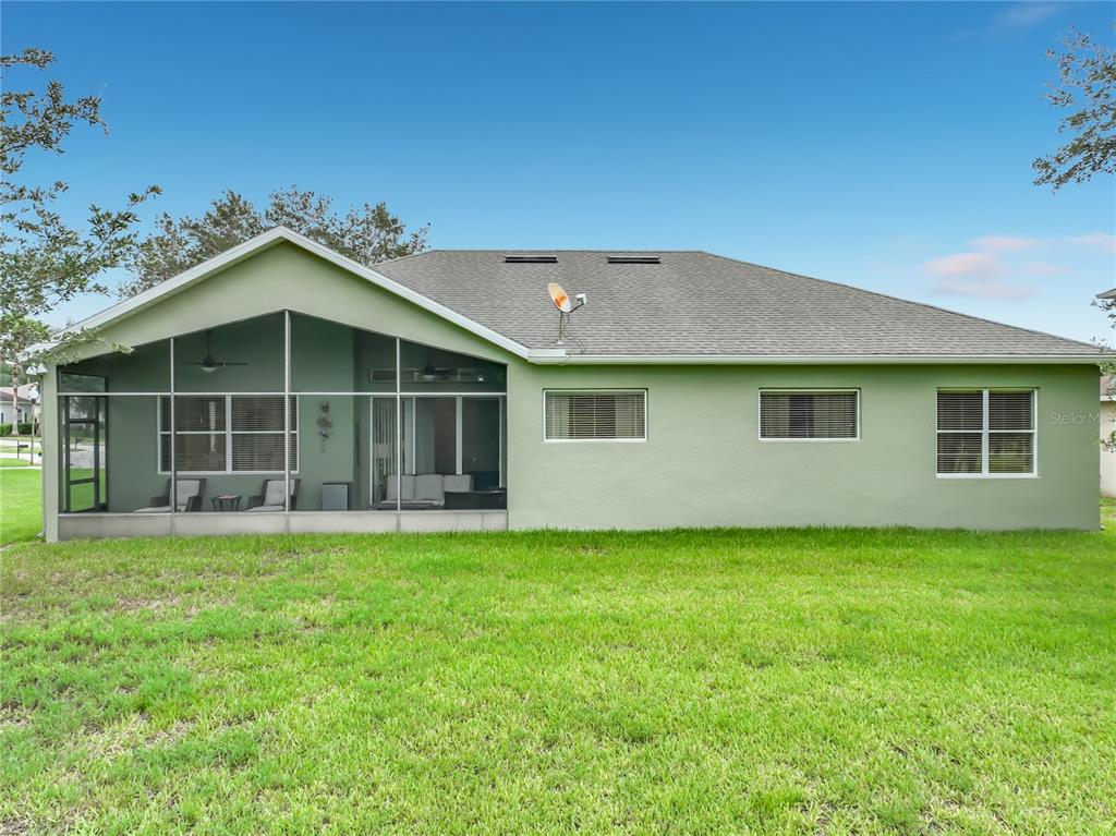 The rear exterior of a light green house features a screened-in patio and three windows — 3678 PEACEPIPE WAY, CLERMONT, FL