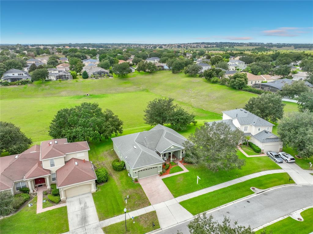 An aerial view shows three suburban houses with green lawns bordering a large open field — 3678 PEACEPIPE WAY, CLERMONT, FL