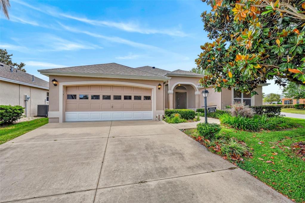 A single-story house with a beige stucco exterior, a two-car garage, and a concrete driveway — 2612 MORVEN PARK WAY, THE VILLAGES, FL