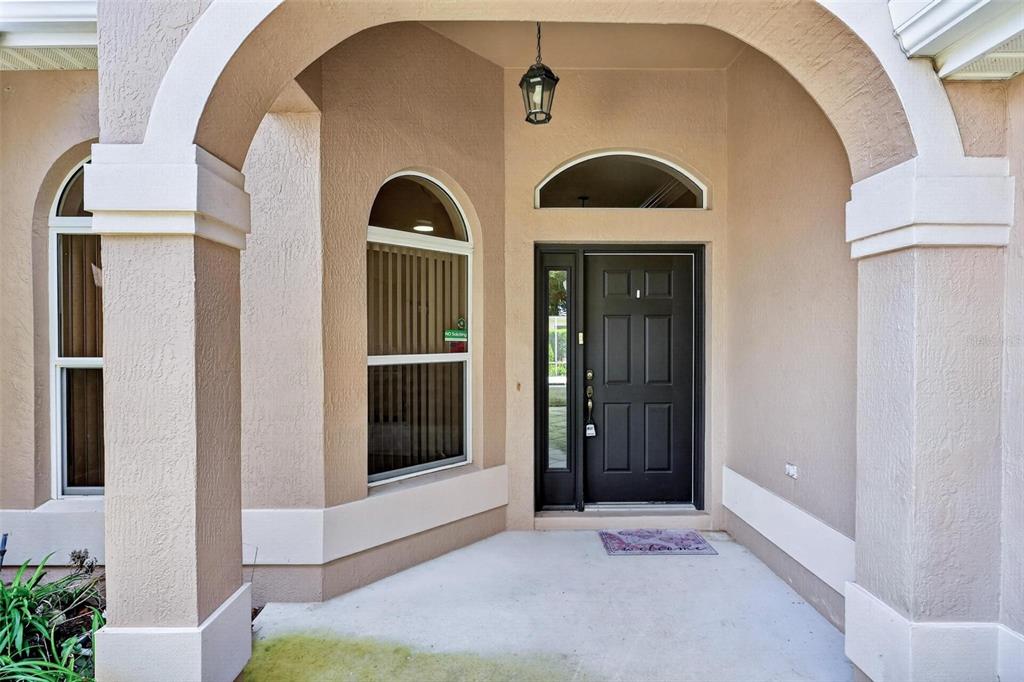A covered front porch features a dark front door, arched windows, and beige stucco walls — 2612 MORVEN PARK WAY, THE VILLAGES, FL