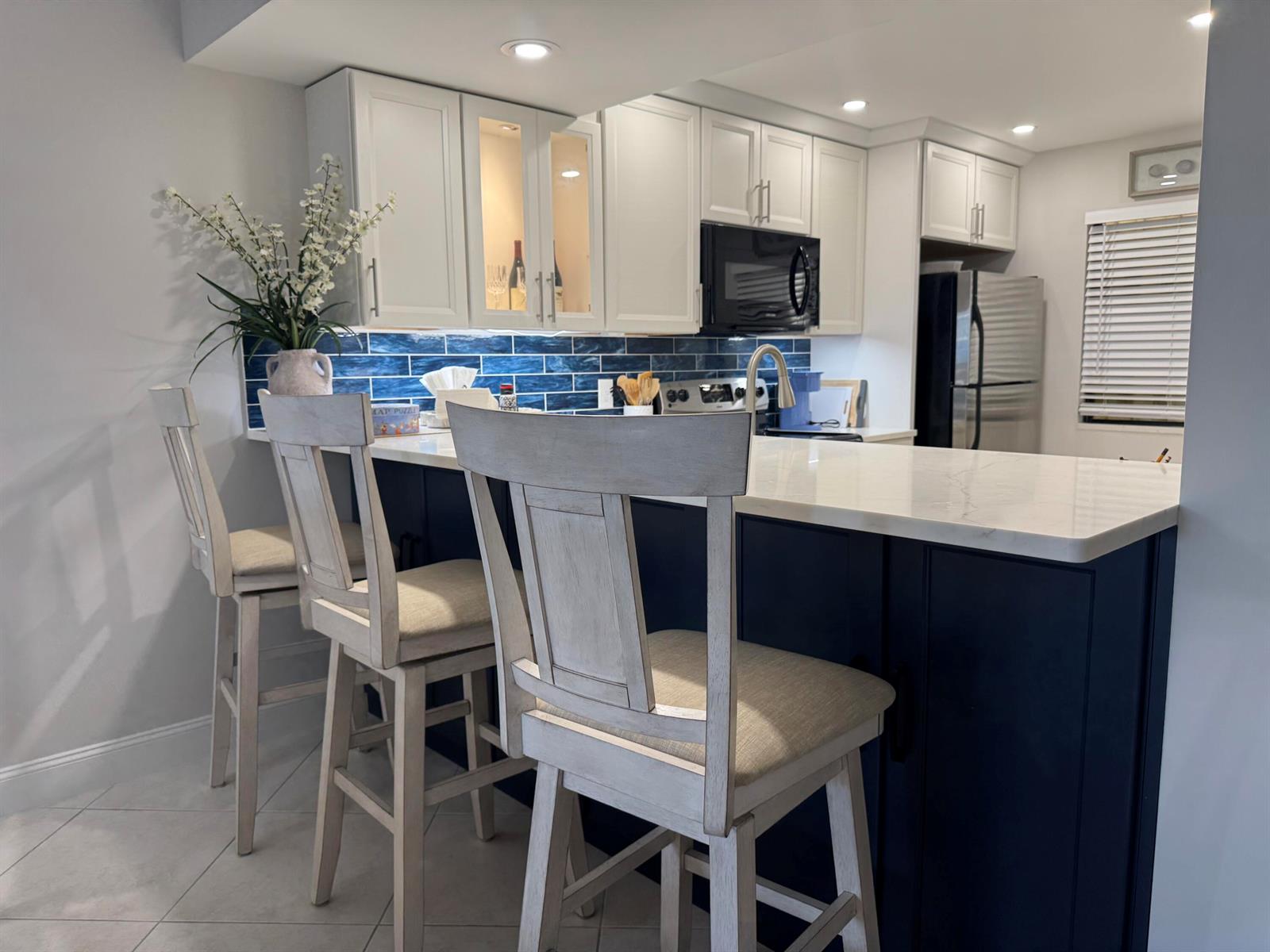 A kitchen features white upper cabinets, dark blue lower cabinets, a blue tile backsplash, and barstools — 401 Ocean Bluffs Boulevard # 303, Jupiter FL 33477, JUPITER, FL