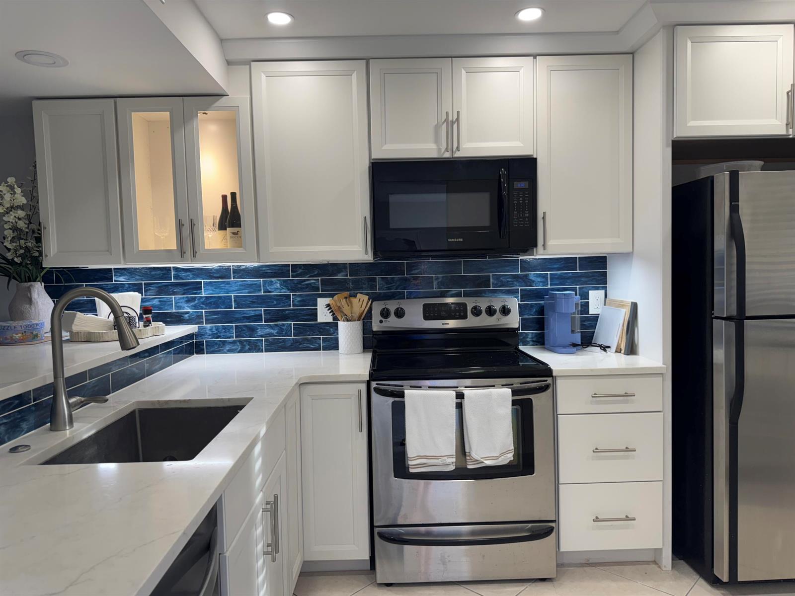 A kitchen features white cabinets, stainless steel appliances, a blue tiled backsplash, and quartz countertops — 401 Ocean Bluffs Boulevard # 303, Jupiter FL 33477, JUPITER, FL