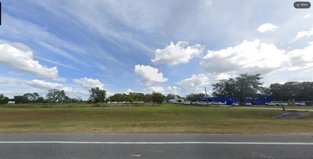 A wide, grassy vacant lot sits alongside a paved road with trees and buildings nearby — N/A, POLK CITY, FL