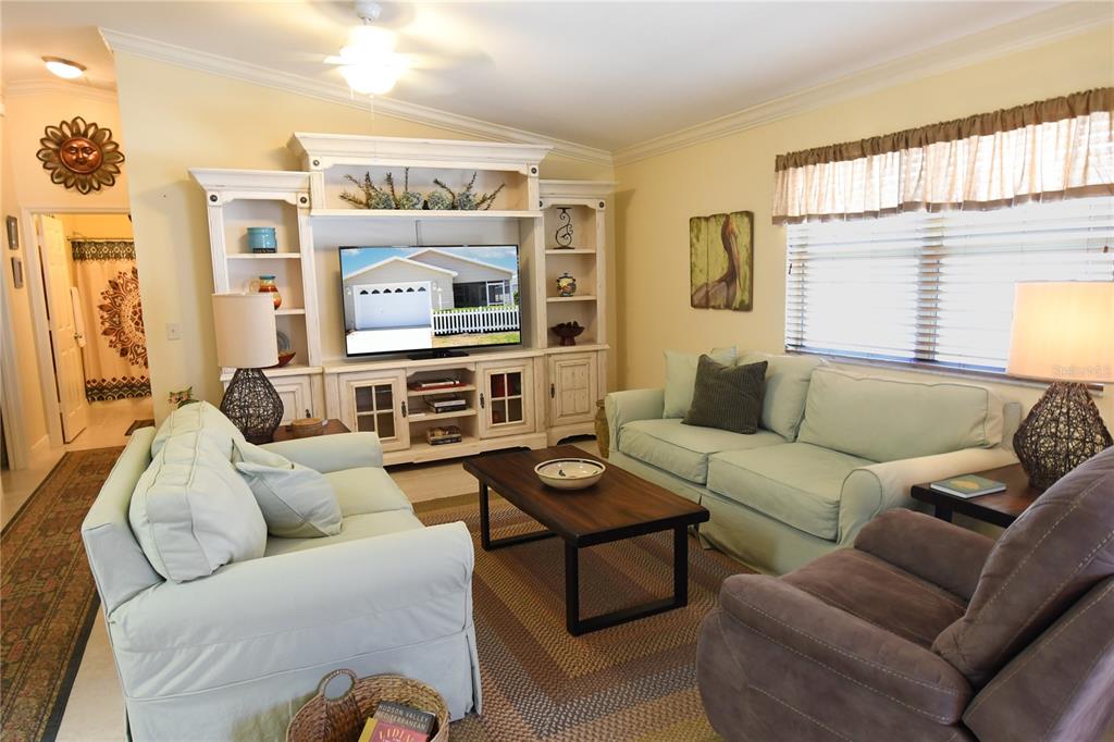 A living room features light blue sofas, a wooden coffee table, and a white entertainment center — 2372 TRAVIS PLACE, THE VILLAGES, FL