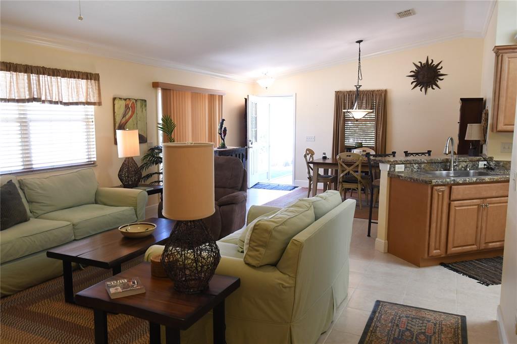 An open-concept living room and kitchen area with light-colored sofas, wood furniture, and tile flooring — 2372 TRAVIS PLACE, THE VILLAGES, FL