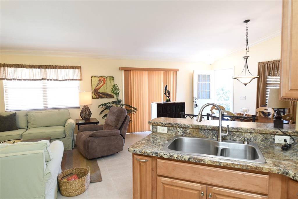A kitchen with granite countertops and a double sink overlooks a living room area — 2372 TRAVIS PLACE, THE VILLAGES, FL