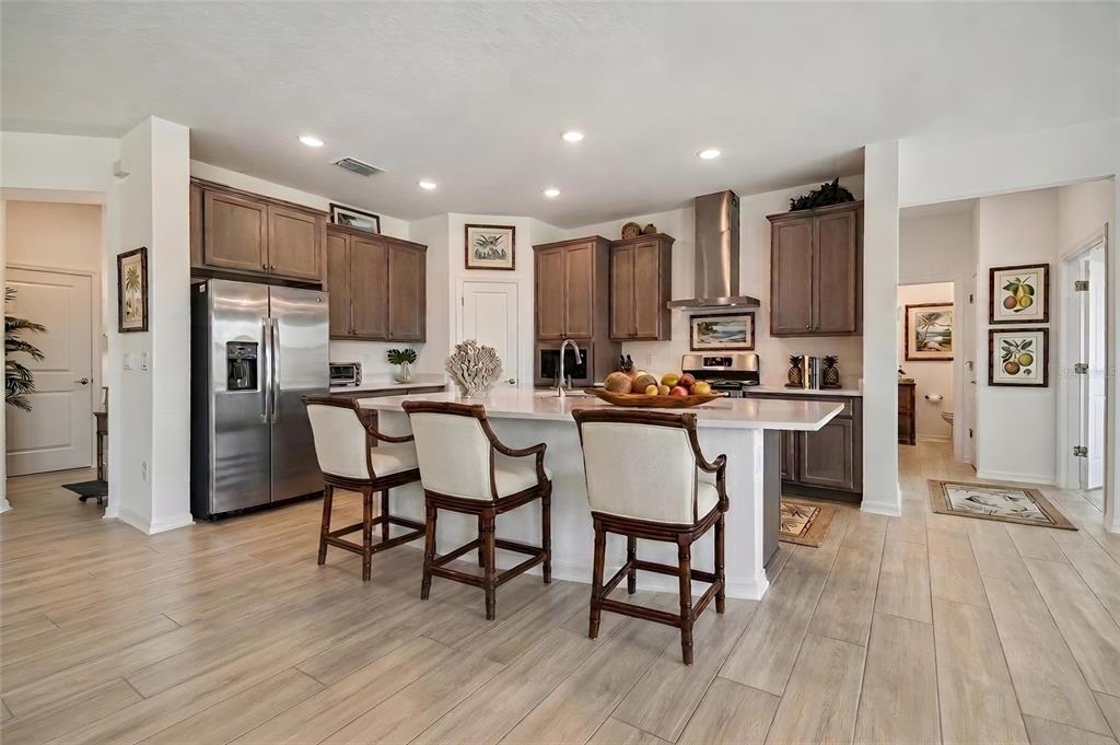 A kitchen features a white island with three chairs, stainless appliances, and wood-toned cabinetry — 5108 JENNINGS TRAIL, BROOKSVILLE, FL