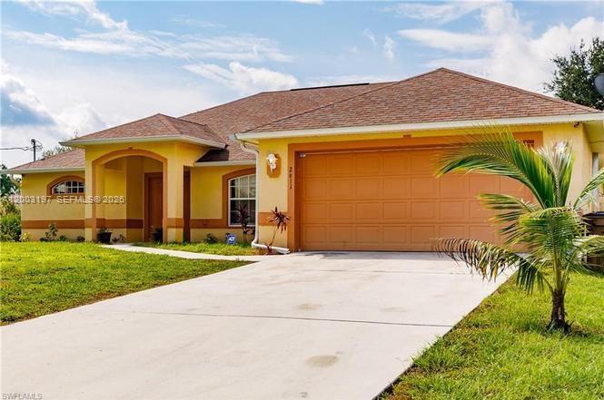 A yellow single-story house features a two-car garage and a concrete driveway — 2611 65 st, Lehigh Acres FL 33971, LEHIGH ACRES, FL