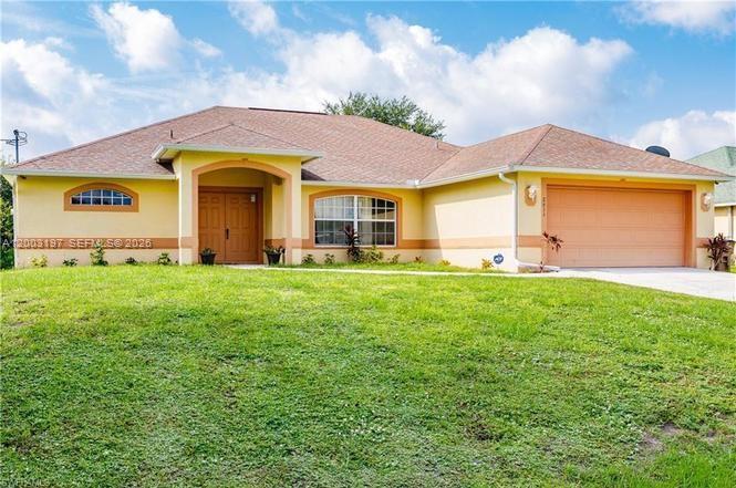 A single-story house with a yellow exterior, a brown shingled roof, and a two-car garage — 2611 65 st, Lehigh Acres FL 33971, LEHIGH ACRES, FL