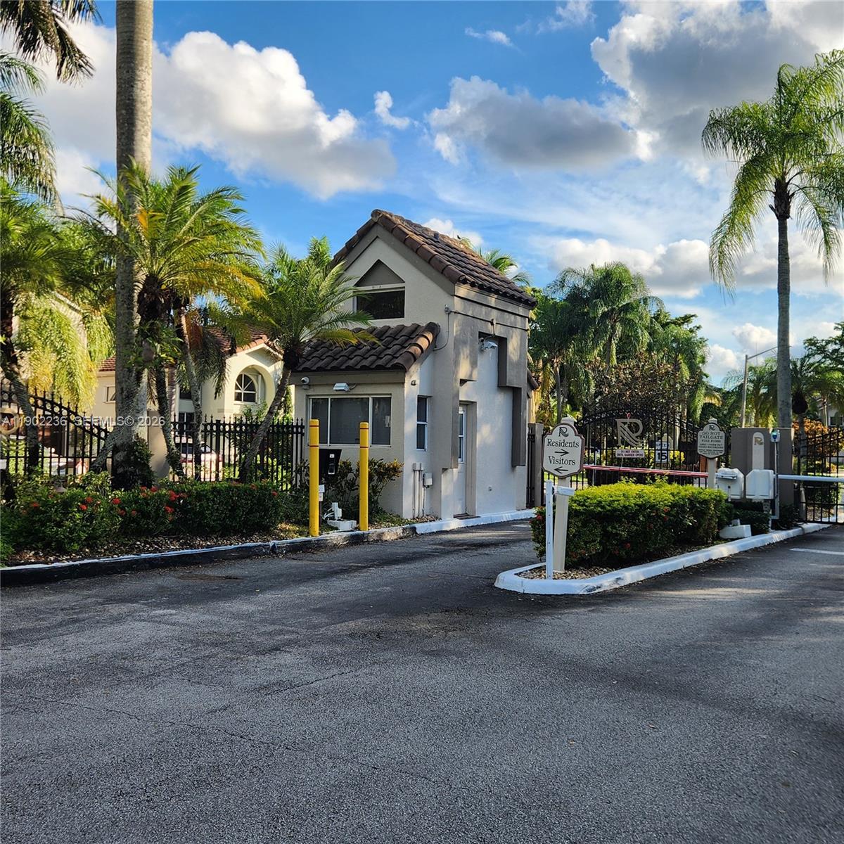 A gated community entrance featuring a guardhouse, palm trees, and a paved driveway — 11281 Reveille Rd, Cooper City FL 33026, COOPER CITY, FL