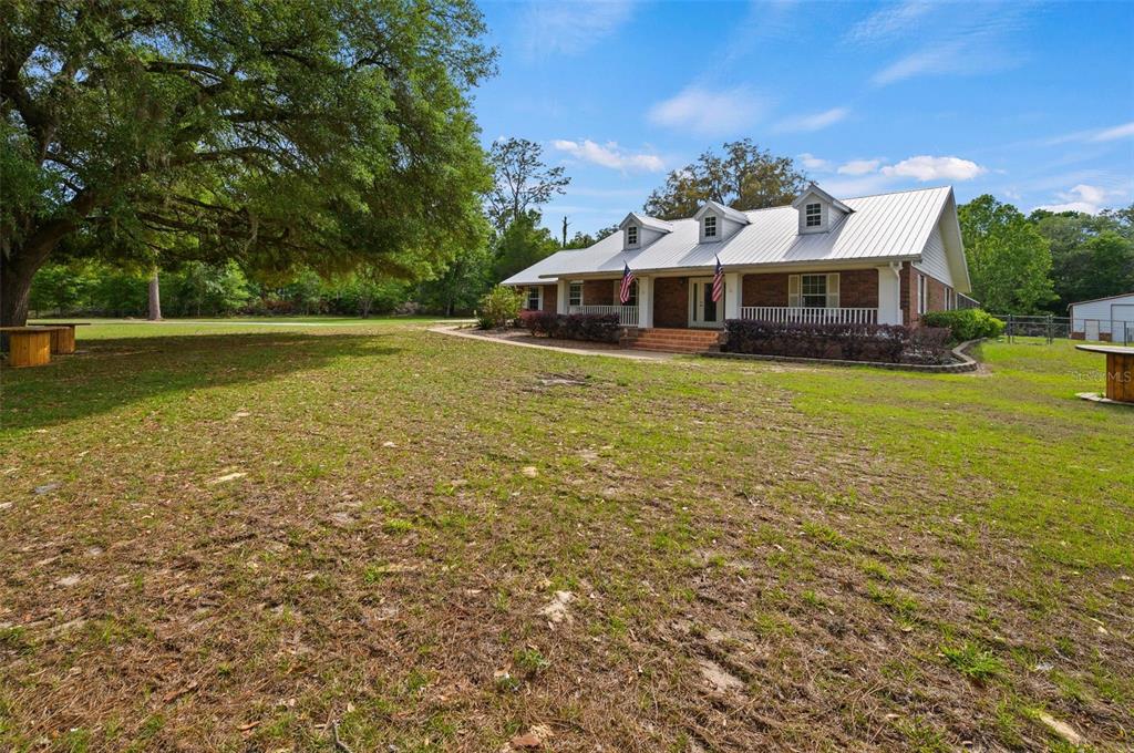 A brick house with a metal roof and dormer windows sits on a grassy lot — 6459 SE COUNTY ROAD 337, NEWBERRY, FL