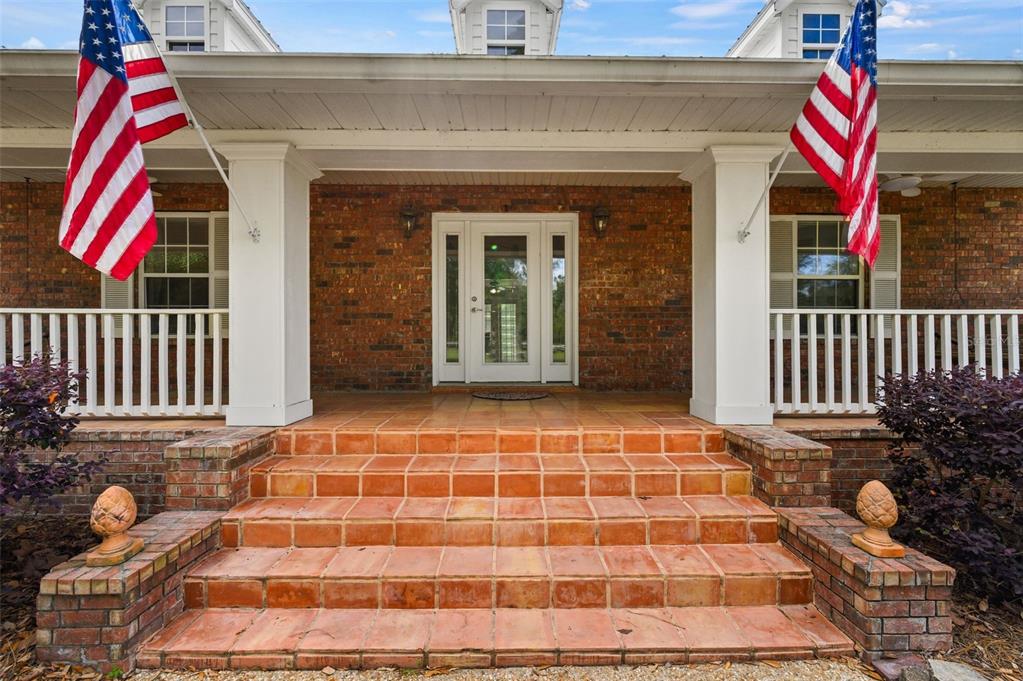 A brick house features a covered front porch with two American flags and tiled steps — 6459 SE COUNTY ROAD 337, NEWBERRY, FL