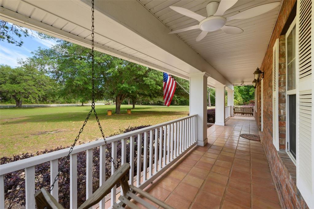 A covered porch with tile flooring, white railings, a ceiling fan, and a hanging swing — 6459 SE COUNTY ROAD 337, NEWBERRY, FL